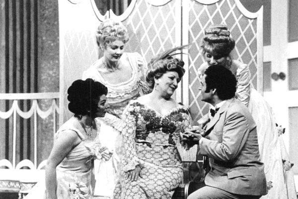 A man and three women circle around the woman with a feather in her hair as they listen to her sing