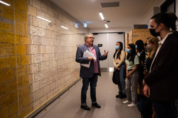 Stuart Maunder in front of the Signature wall at Her Majesty's Theatre leading a school group on a behind the scenes tour