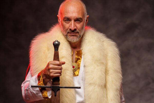 Regal man holding sword wearing red robes with gold and fur trim