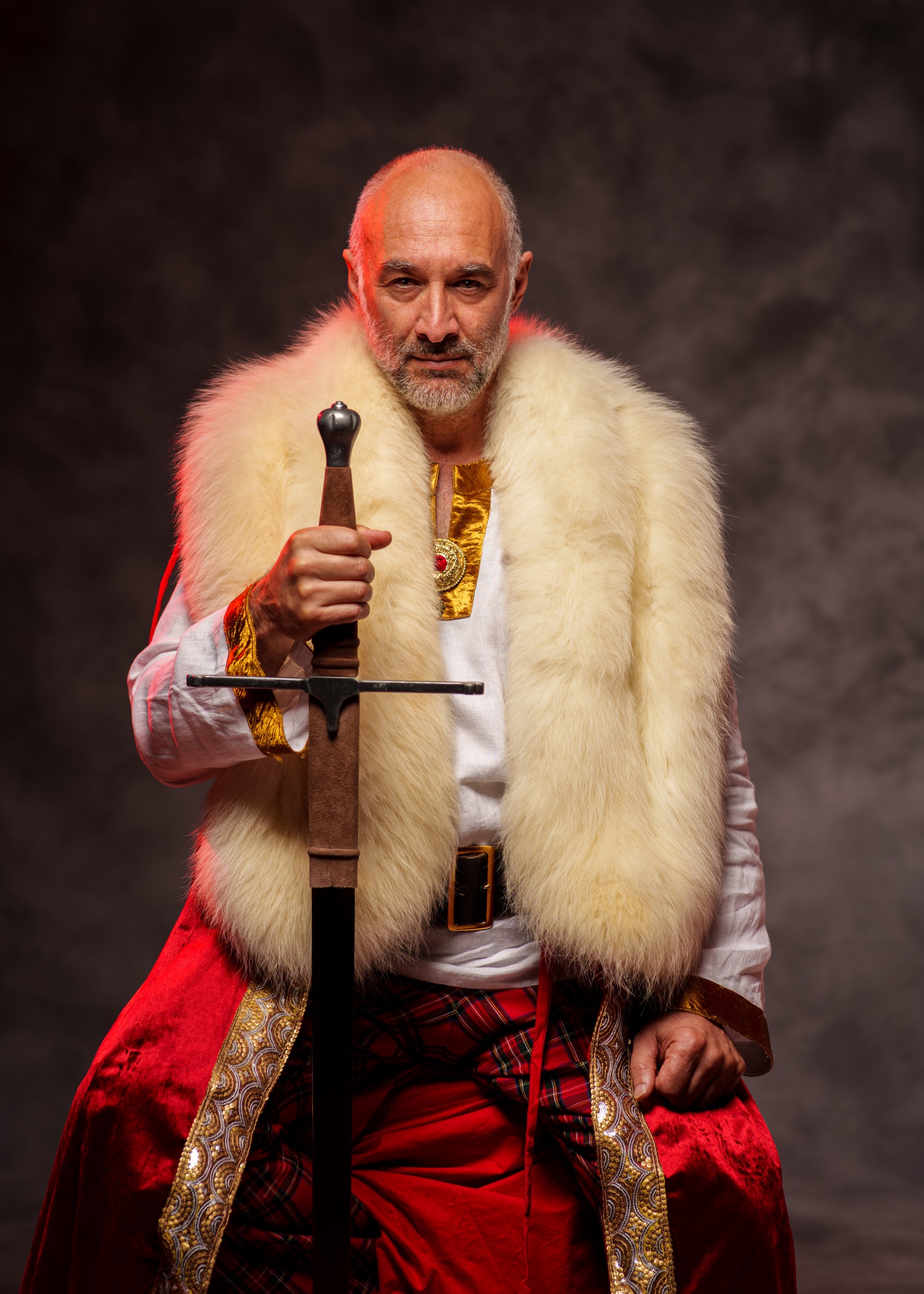 Regal man holding sword wearing red robes with gold and fur trim